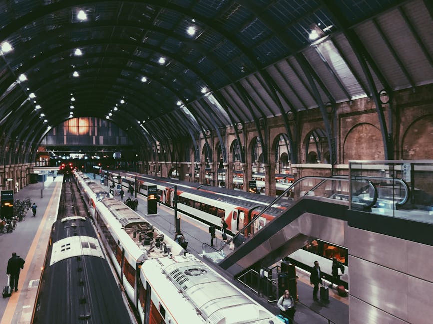 Inside a large, enclosed train station with a high, curved metal and glass arched ceiling illuminated by ceiling lights. The station features multiple railway tracks on the ground level, with several