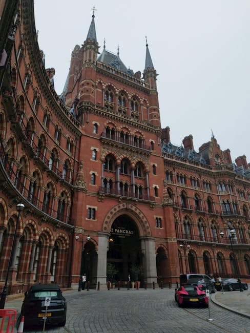 A close-up view of a red brick building with arched windows and a weathered surface, featuring a London Underground roundel sign prominently displayed in the foreground. Above the building, a section 